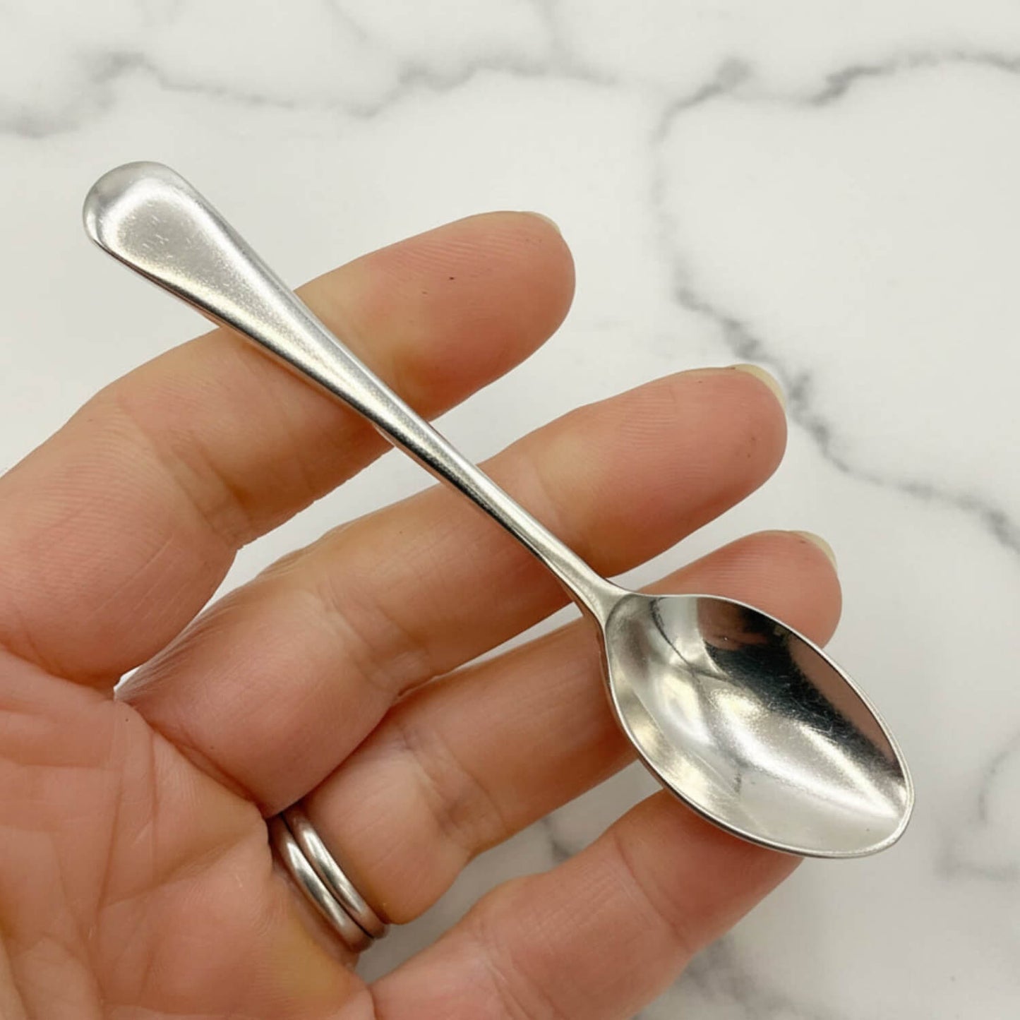 Hand holding a small silver coffee spoon against a marble background