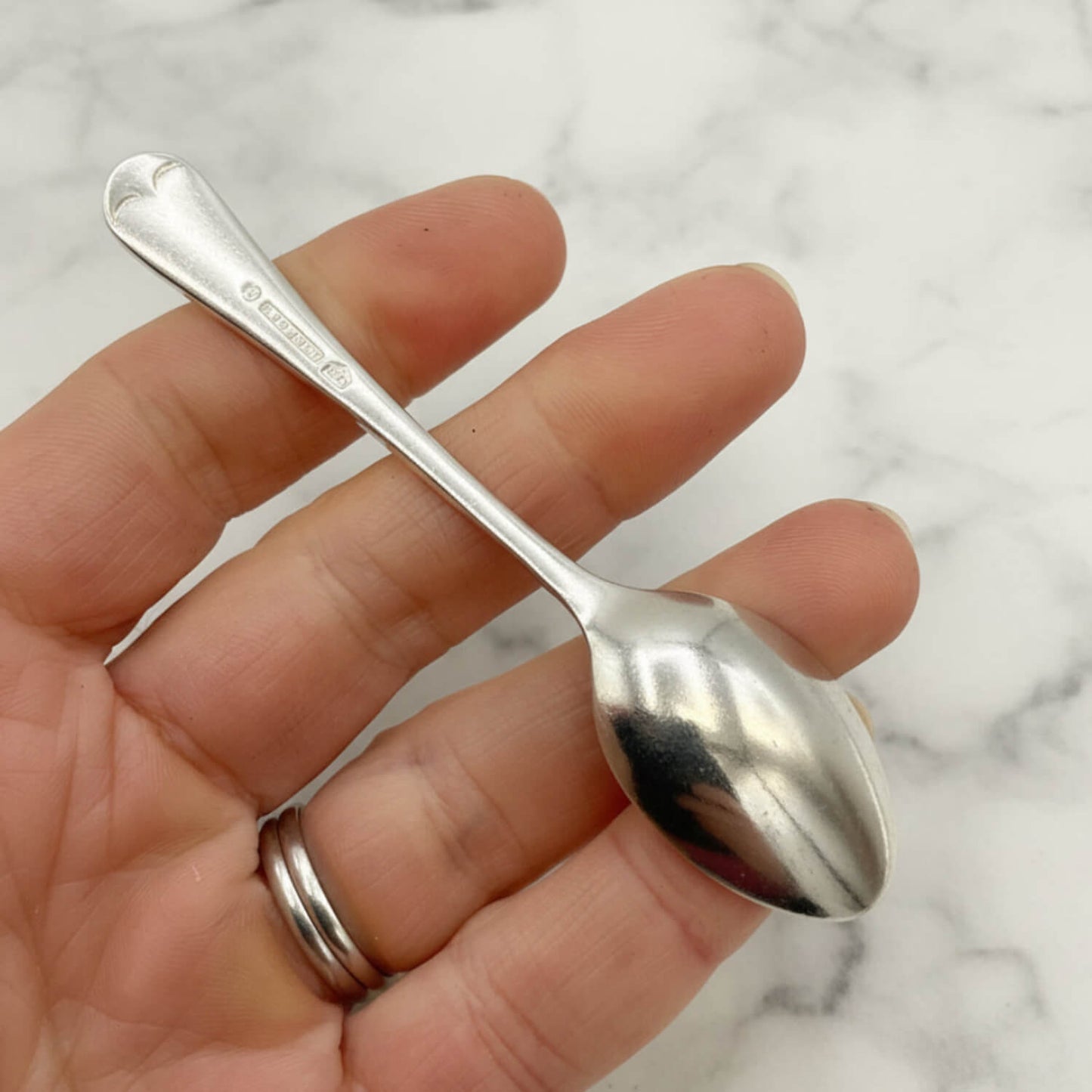 Silver coffee spoon held in a hand against a marble background