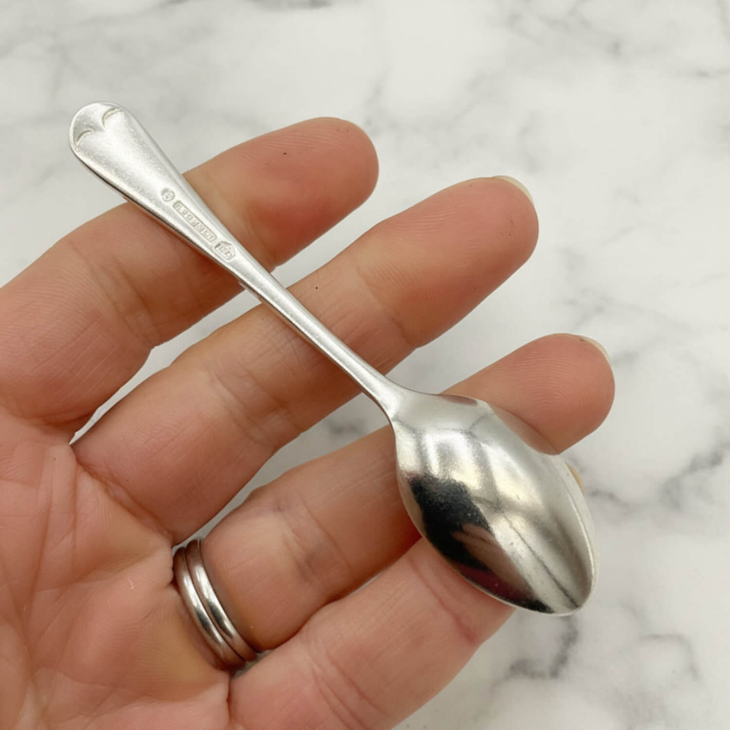Silver coffee spoon held in a hand against a marble background