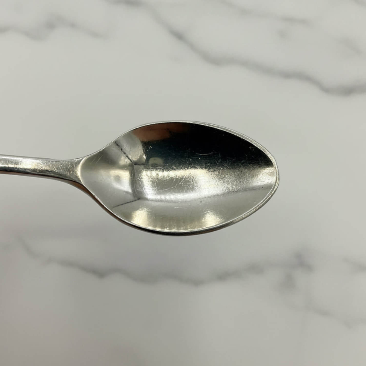 Silver coffee spoon bowl on a marble surface