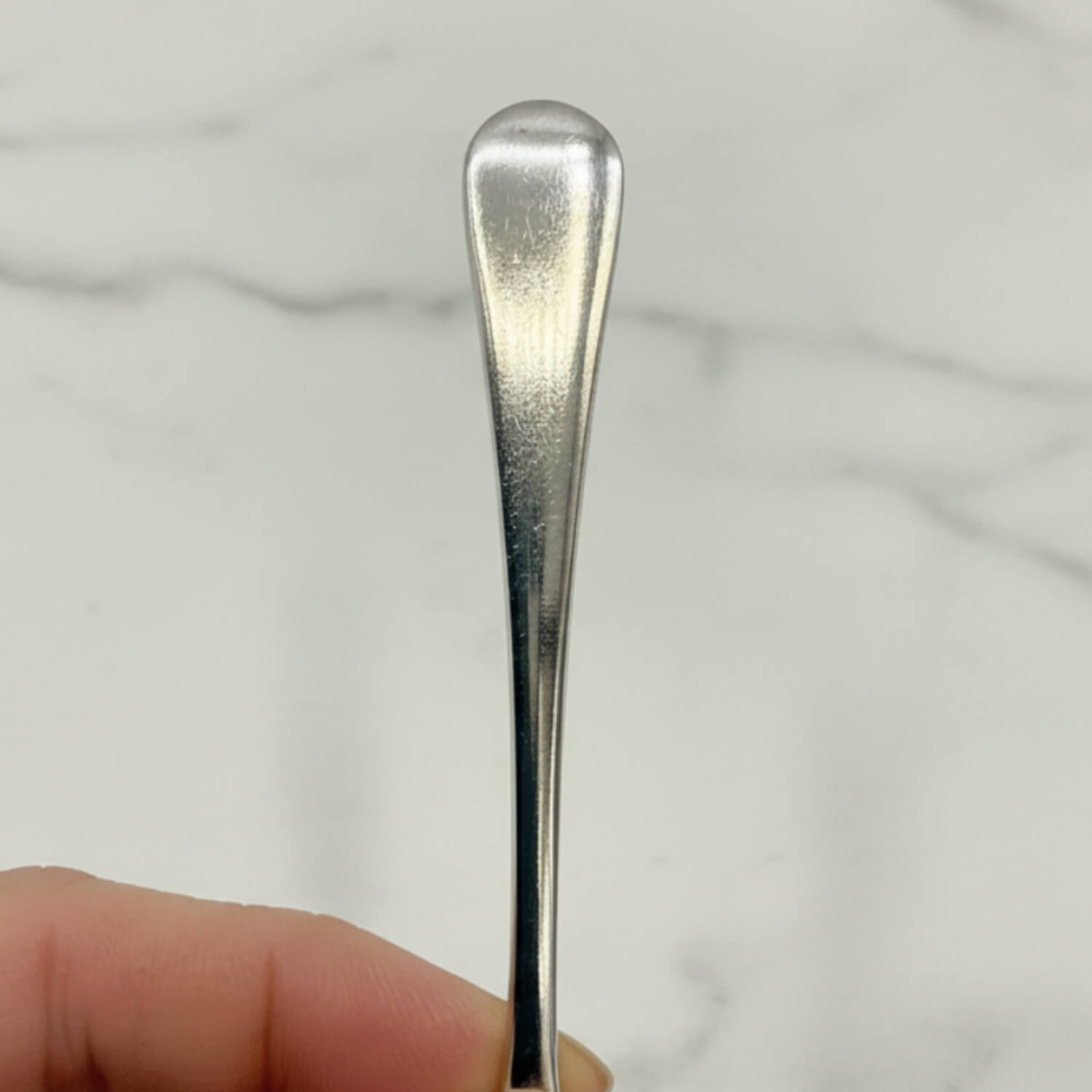 Silver spoon handle held by a hand against a light marble background