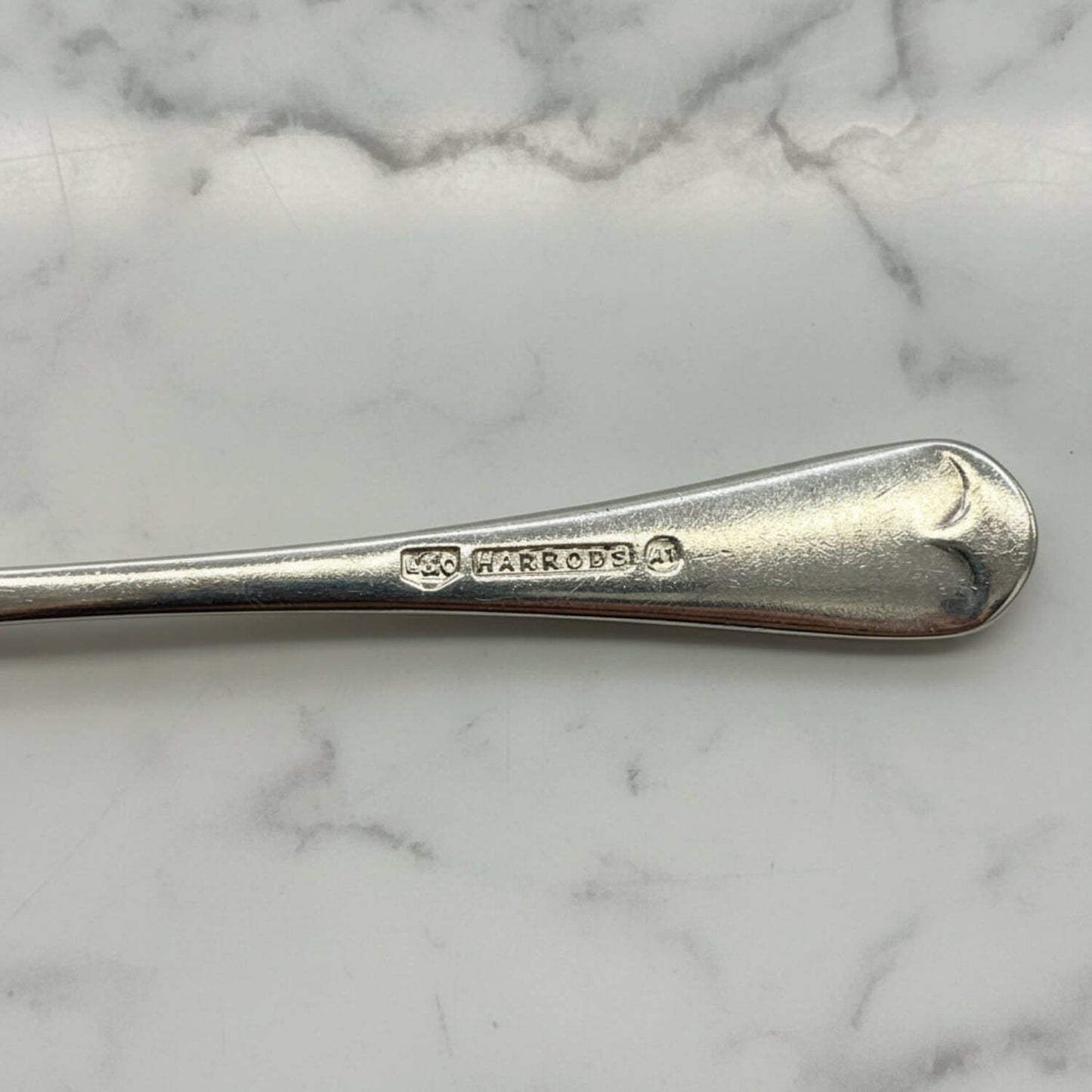 Silver coffee spoon with Harrods branding on a marble surface