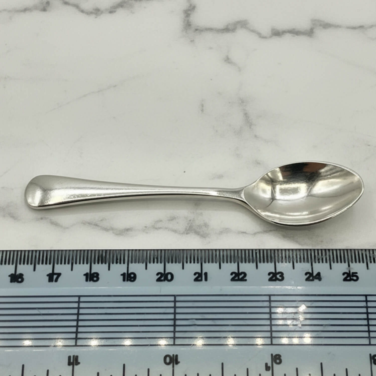 Silver coffee spoon on a marble surface with a ruler for scale