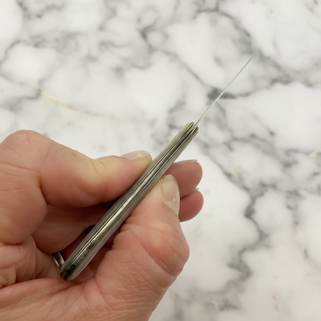Hand holding a fruit knife showing the top of it against a marble background