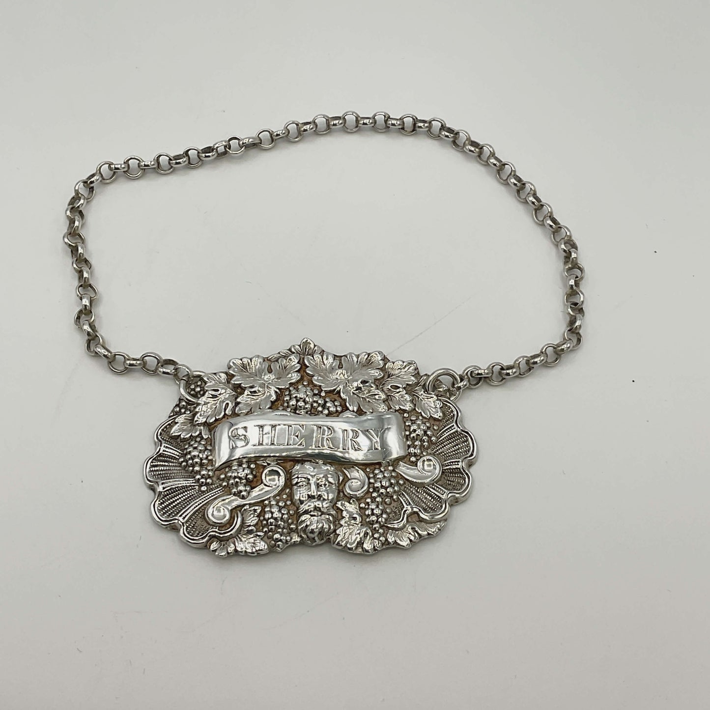 Decorative silver decanter label with 'SHERRY' on a chain against a white background
