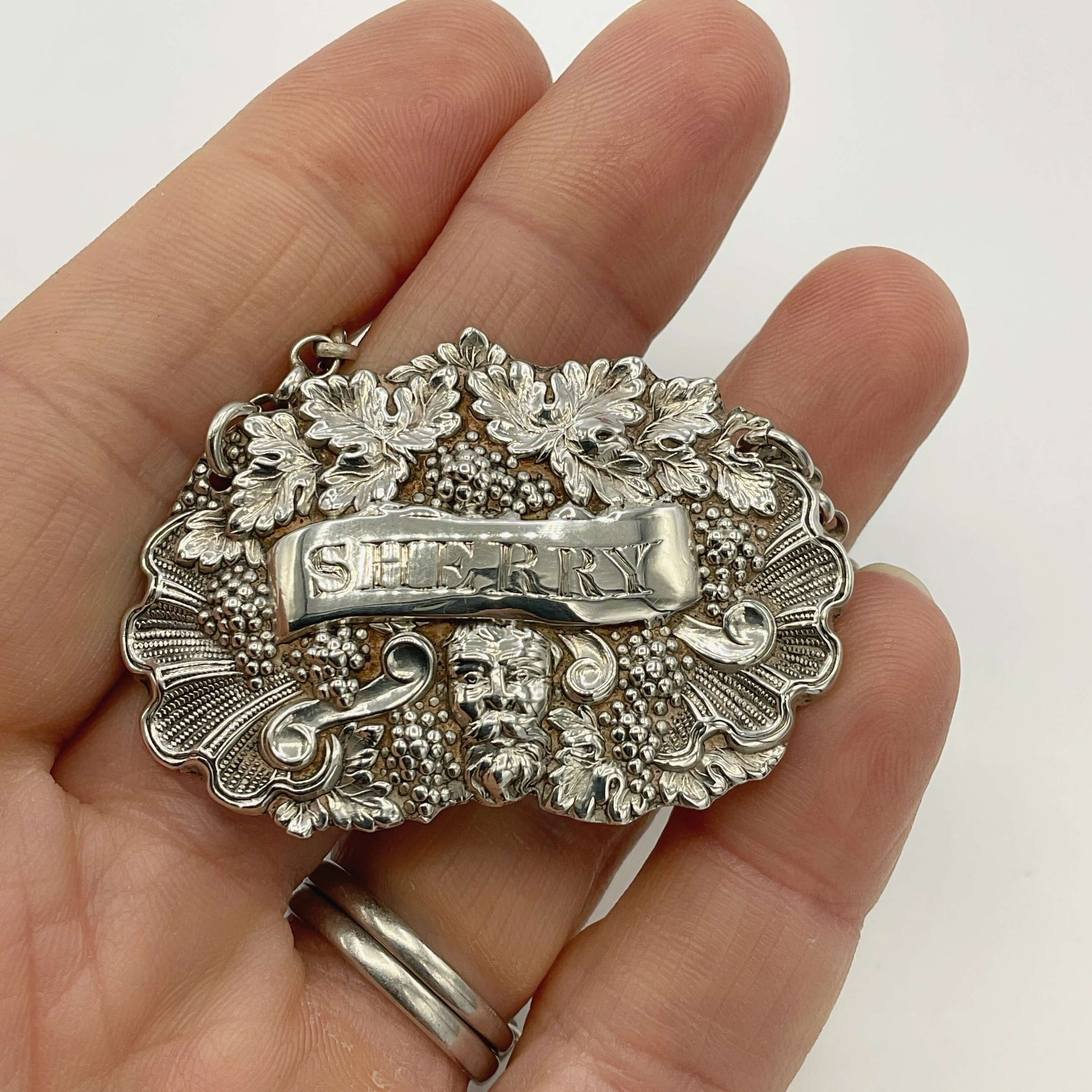 Silver 'SHERRY' decanter label held in a hand against a white background