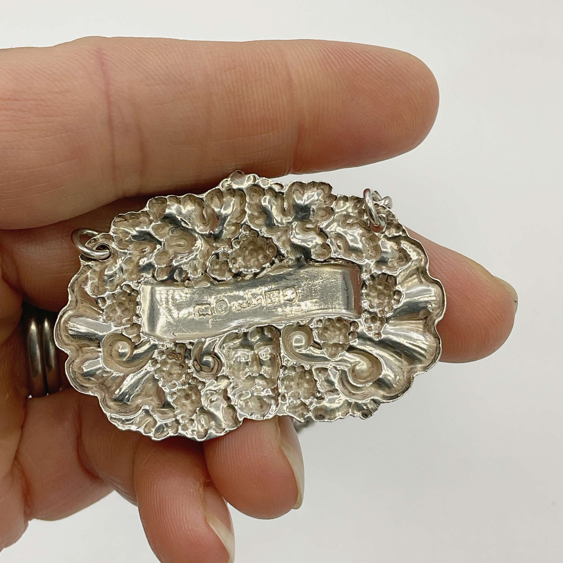 Silver decanter label held by a hand with a plain background