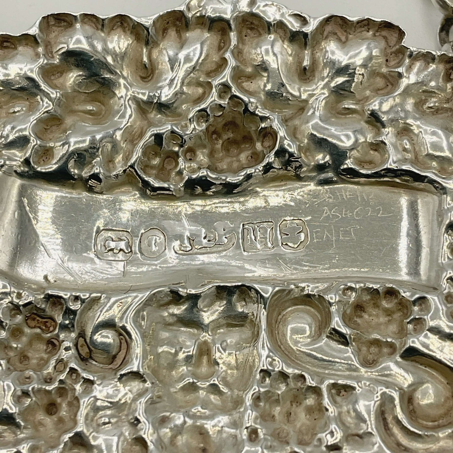 Close-up of a back of a silver decanter label with engraved patterns and visible hallmarks.