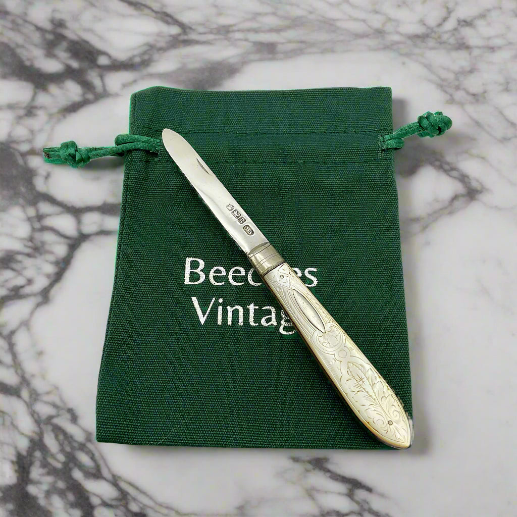 Silver fruit knife with decorative handle on a green drawstring bag labeled Beeches Vintage'.