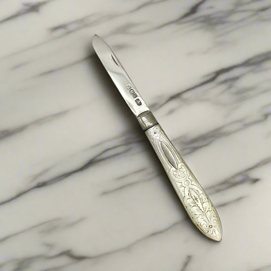 Silver fruit knife with engraved handle on a light marble background