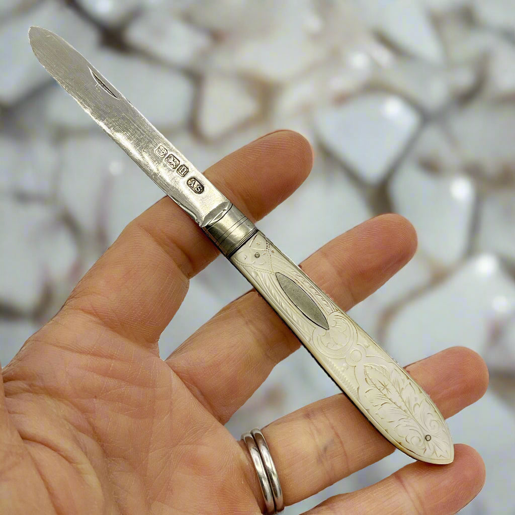 Hand holding a silver fruit knife with engraved handle on a marble background