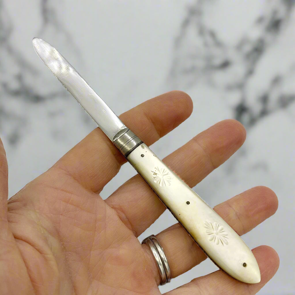 Hand holding a decorative silver fruit knife with an engraved handle against a marble background