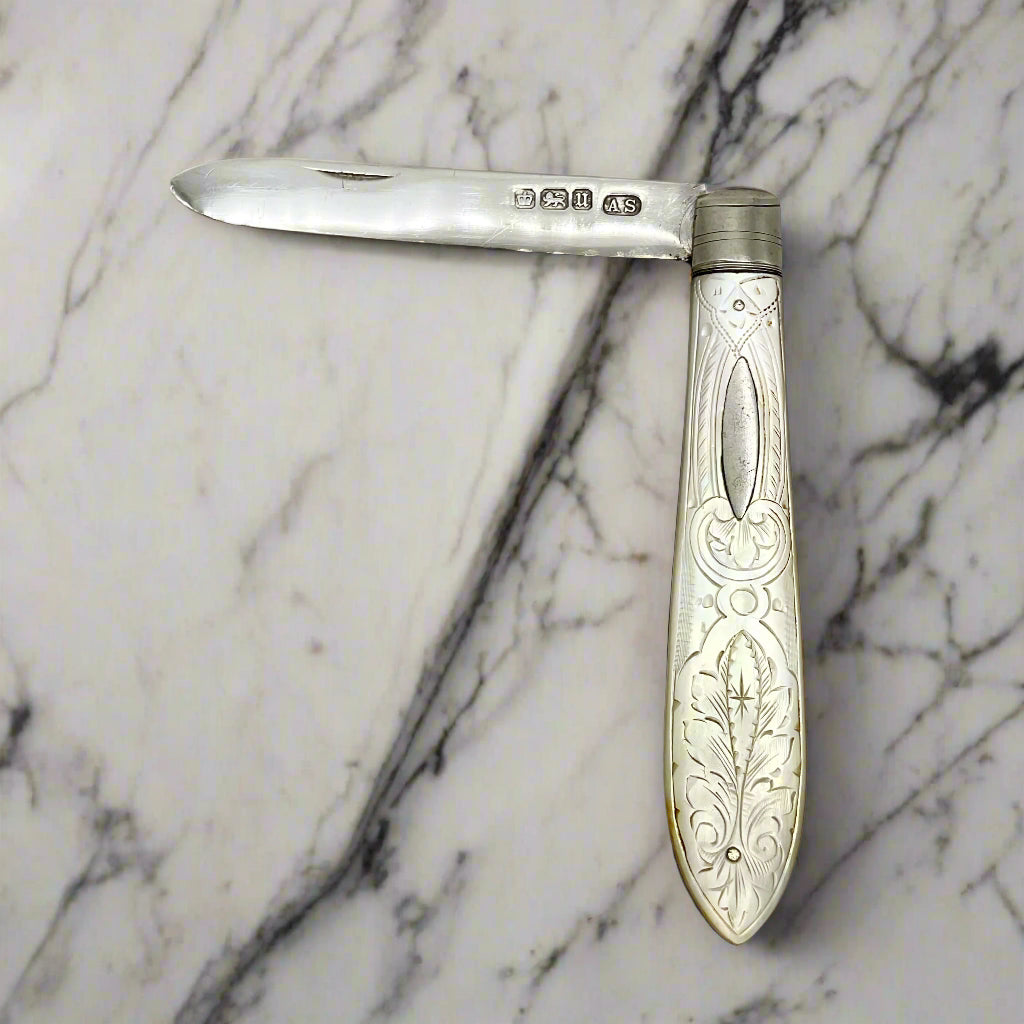 Silver folding knife with engraved handle on a light marble background