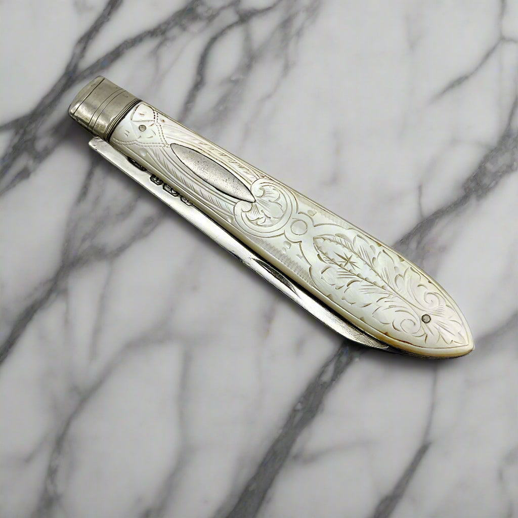 Decorative fruit knife with silver blade and engraved handle on a light marble background