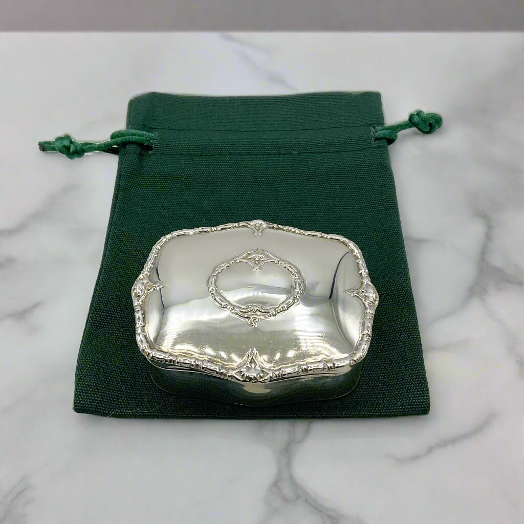 Silver decorative box on a green drawstring bag with a marble background