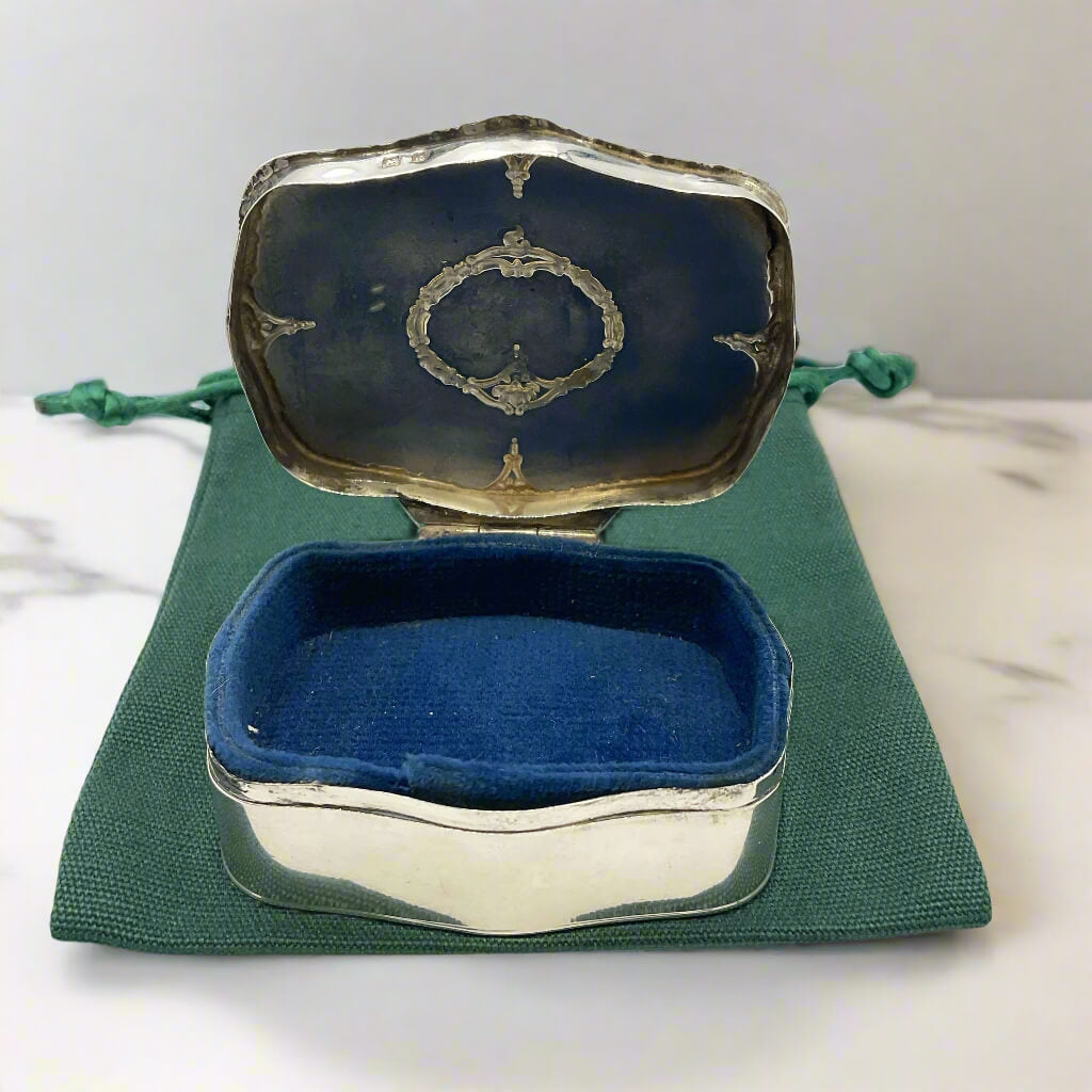 Silver jewelry box with blue interior on a green fabric background
