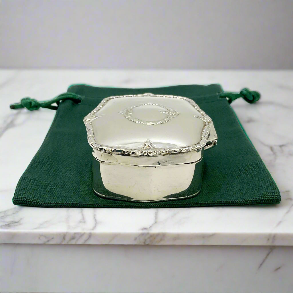 Silver trinket box on a green drawstring bag with a marble background