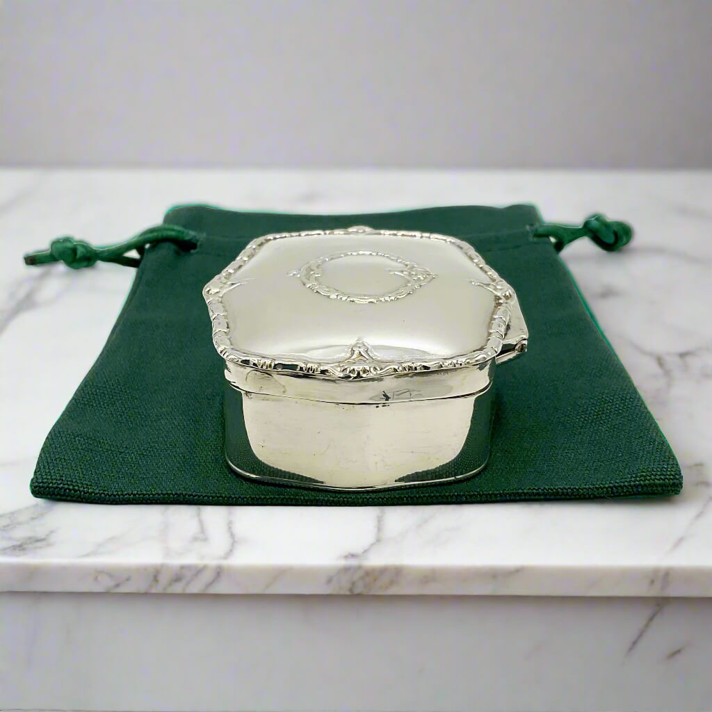 Silver trinket box on a green drawstring bag with a marble surface background