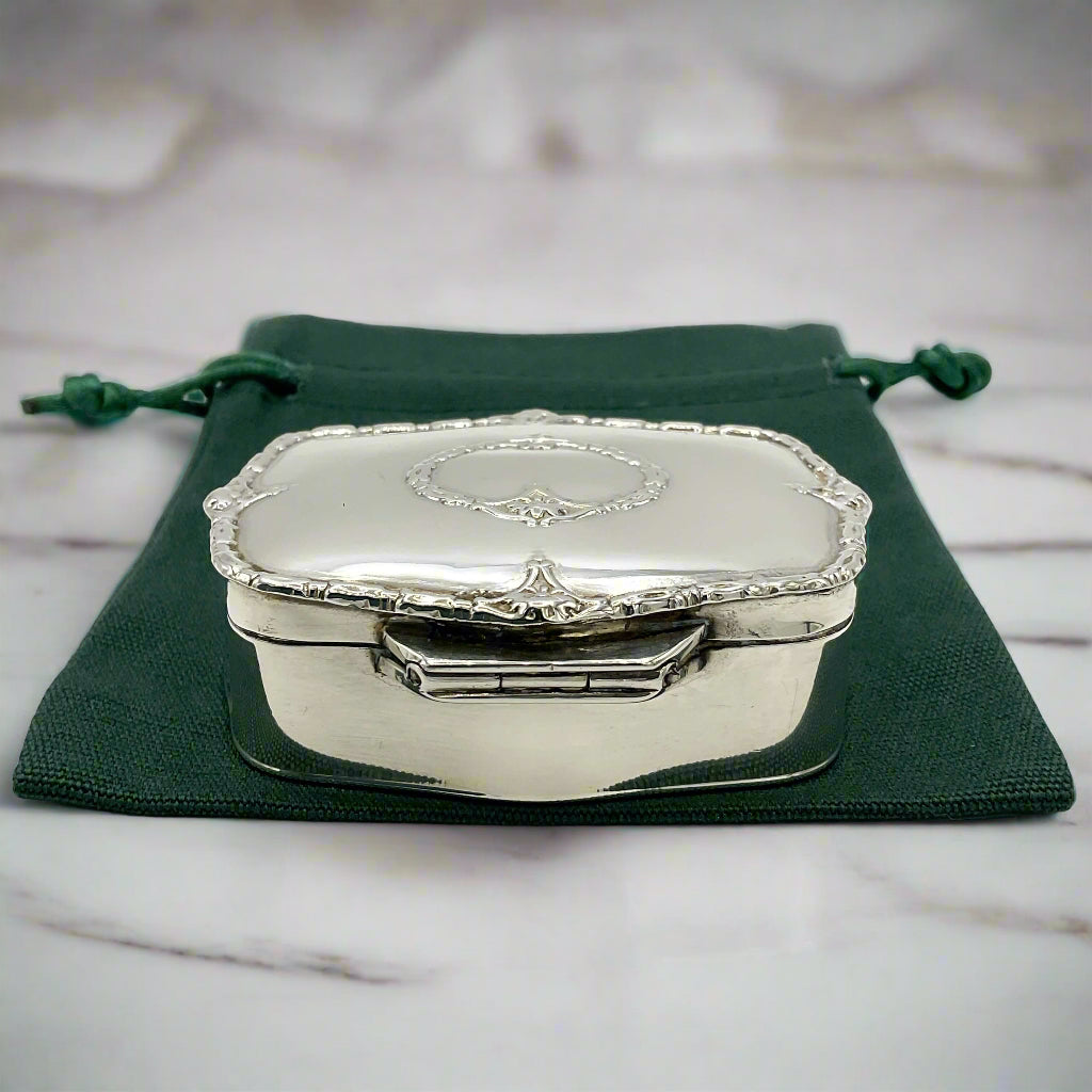 Silver jewelry box with a green drawstring bag on a marble background