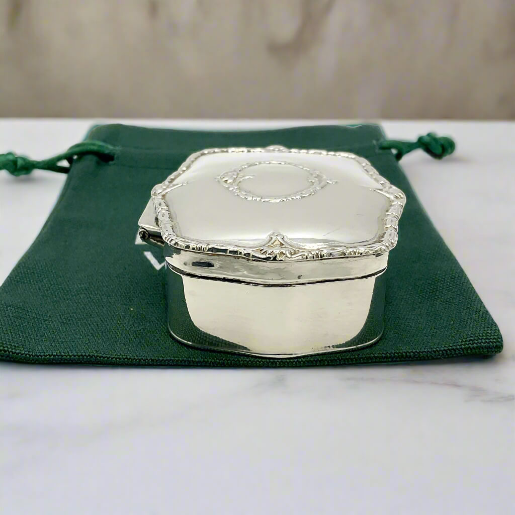 Silver jewelry box on a green drawstring bag with a marble surface background