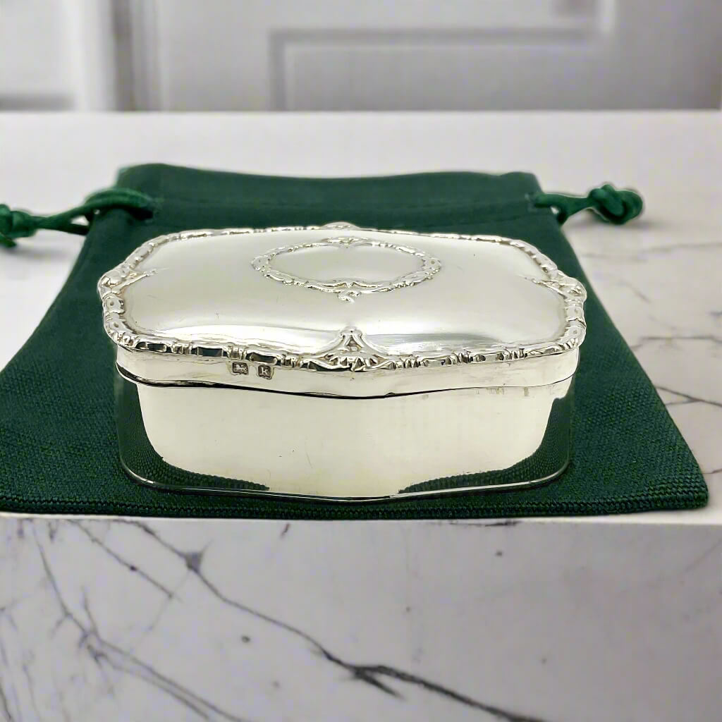 Silver jewelry box on a green fabric pouch with a marble surface background