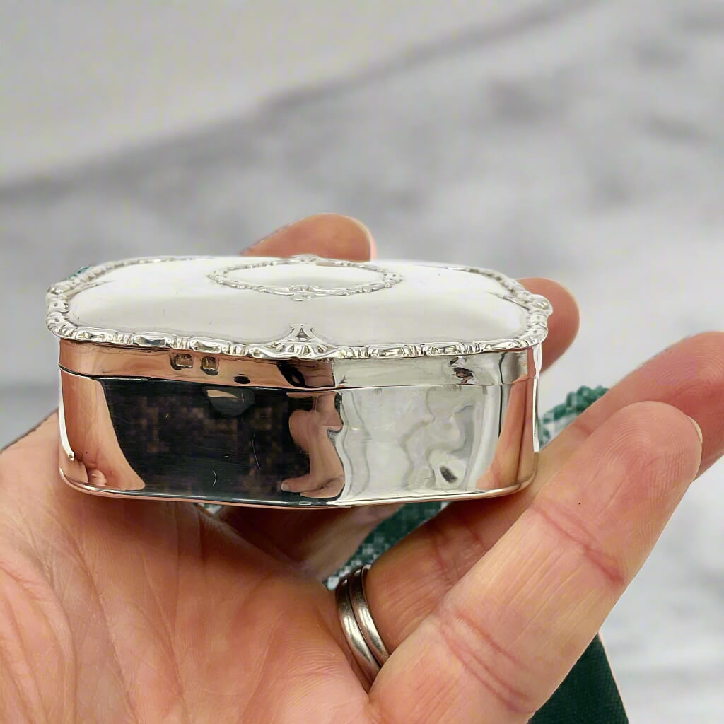 Silver jewelry box held in a hand with a blurred background