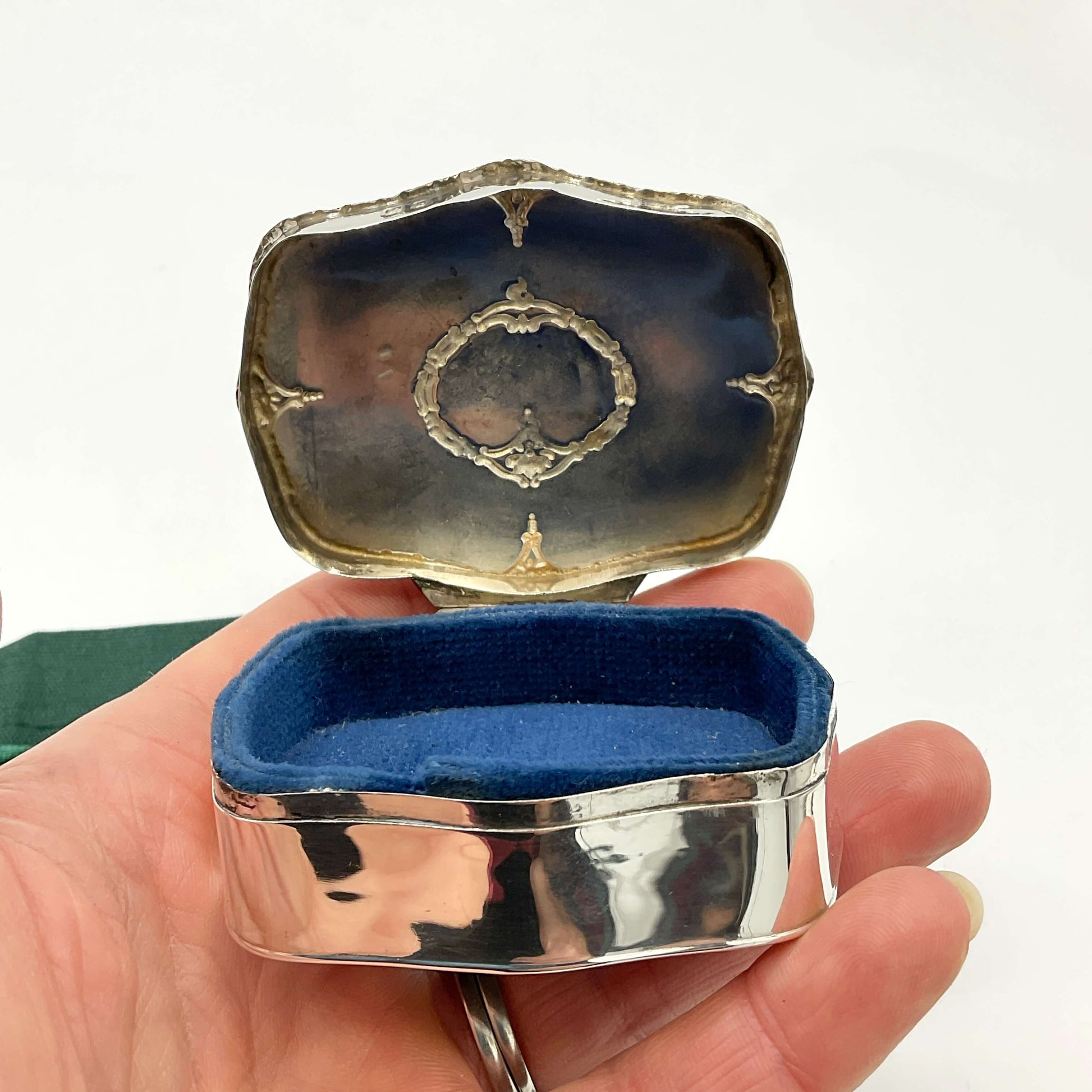 Silver jewelry box with blue interior held in a hand against a white background