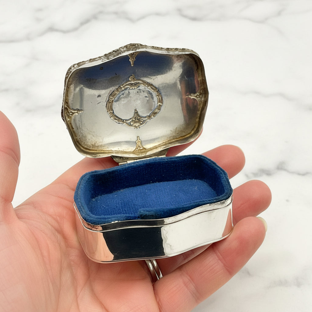 Silver jewelry box with blue interior held in a hand against a marble background