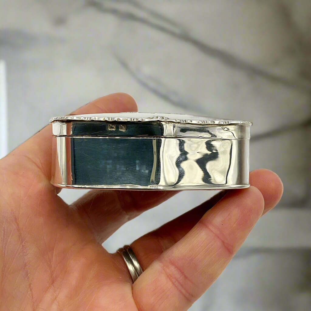 Side view of silver jewellery box held in a hand with a marble background