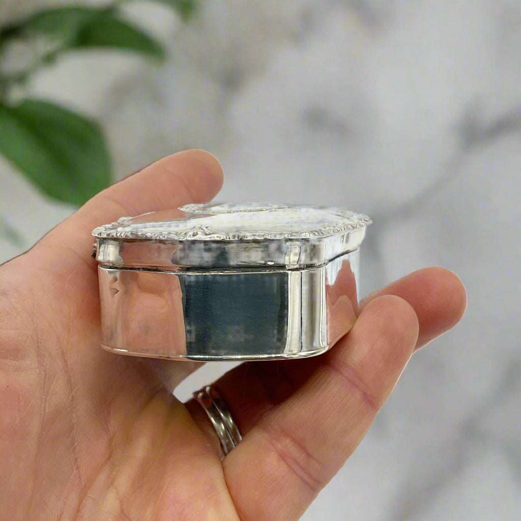Hand holding a small silver jewelry box against a marble background
