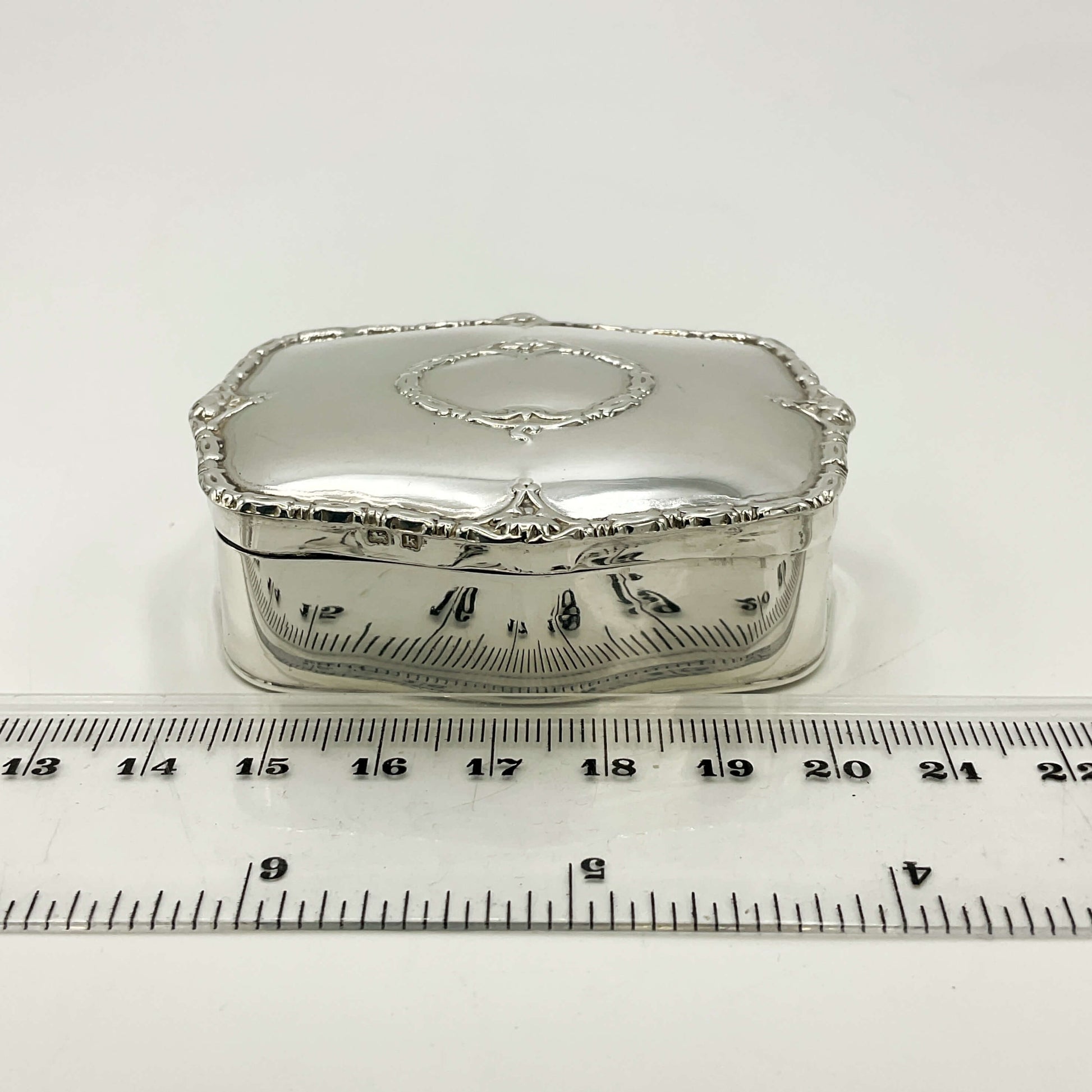 Silver jewelry box with decorative elements on a white background with a ruler for scale.