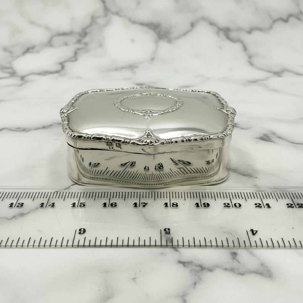 silver jewellery box on a marble surface next to a ruler for scale