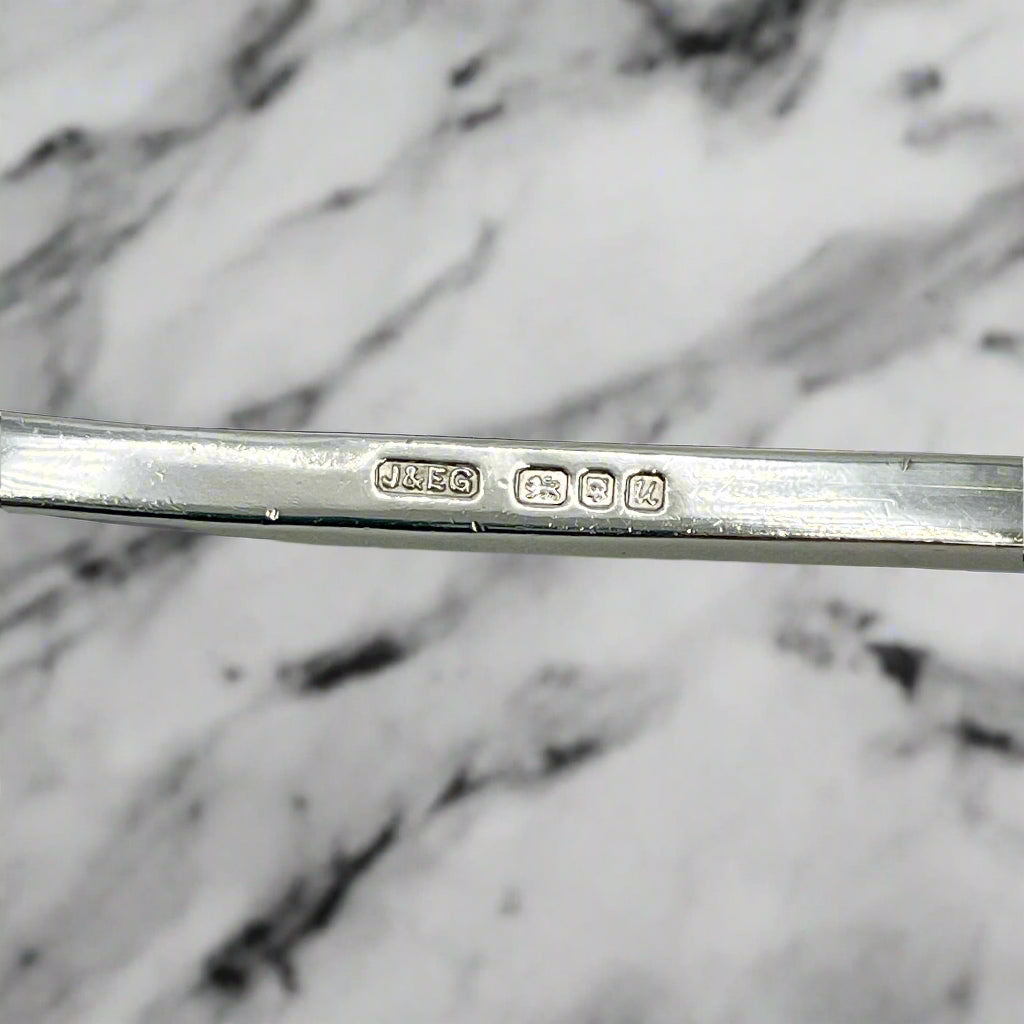 Close-up of a silver spoon with engraved hallmarks on a marble background 