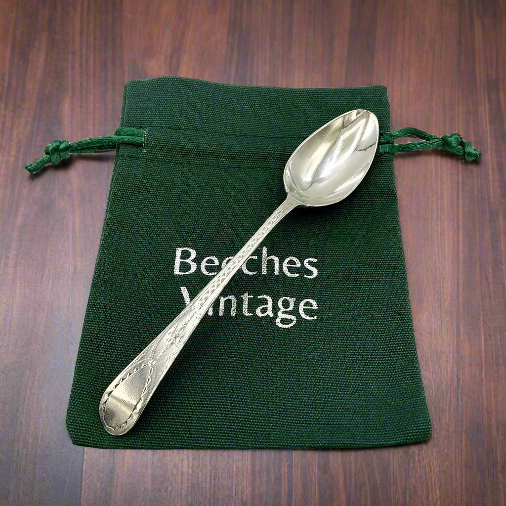 Silver spoon on a green drawstring bag with 'Beeches Vintage' text on a wood table