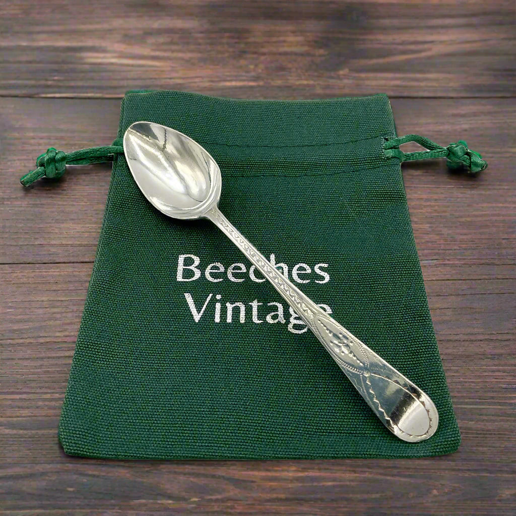 Silver spoon on a green drawstring bag with 'Beeches Vintage' branding on a wood table