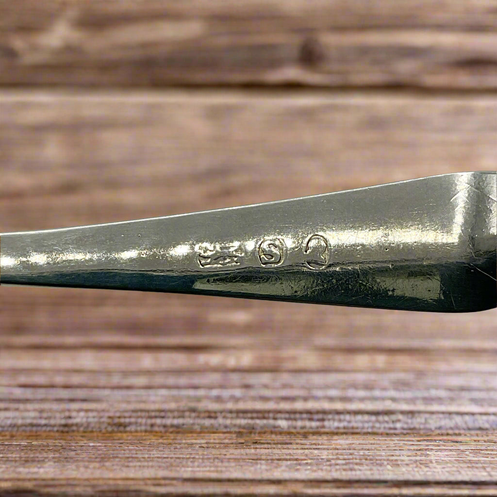 Close-up of a silver spoon with visible hallmarks on a wood background 