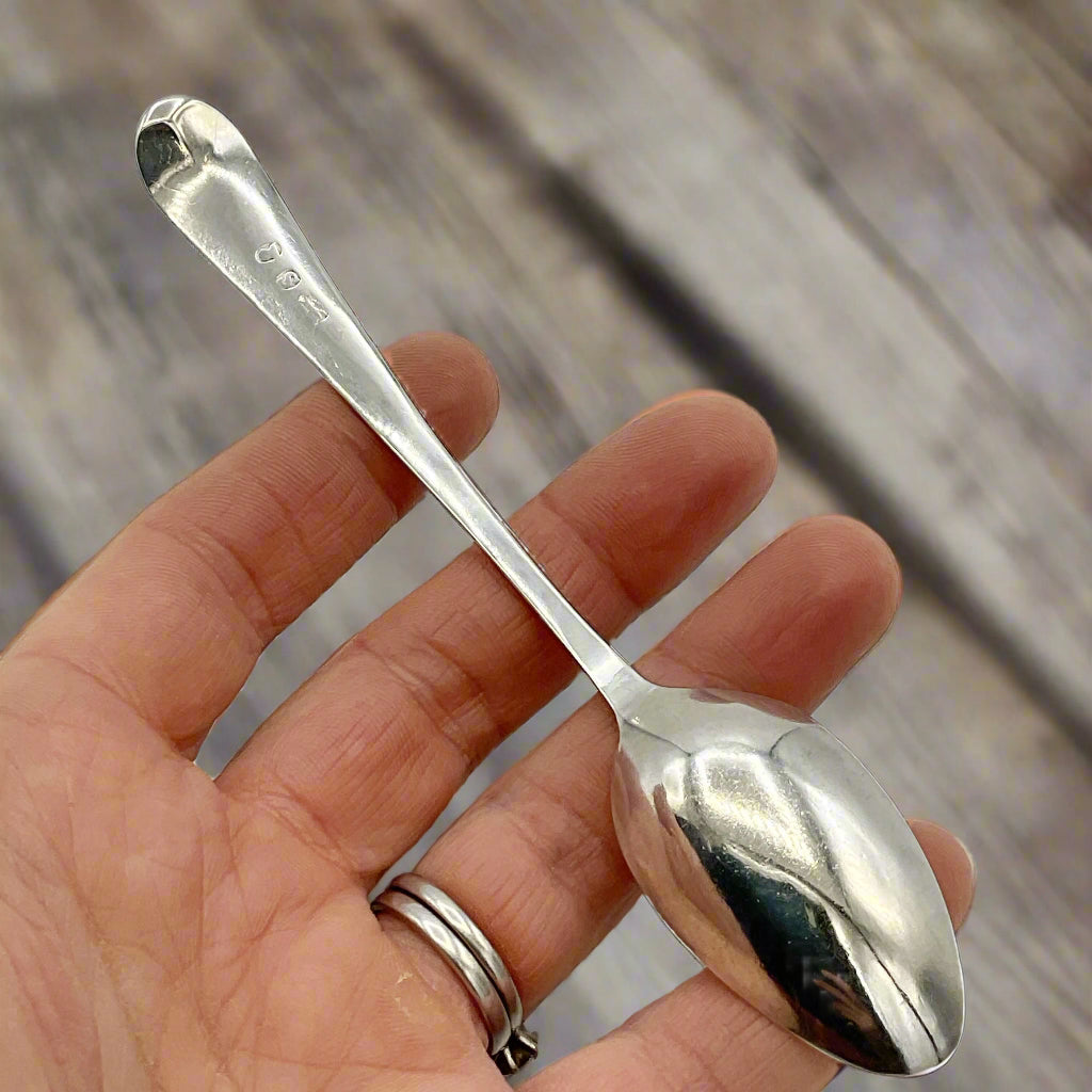 Silver spoon held in a hand against a wood background 