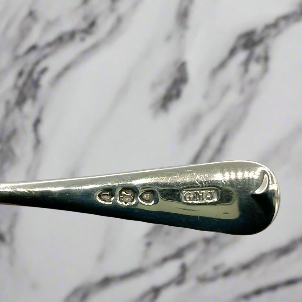 Close-up of a silver spoon with engraved hallmarks on a light marble background 