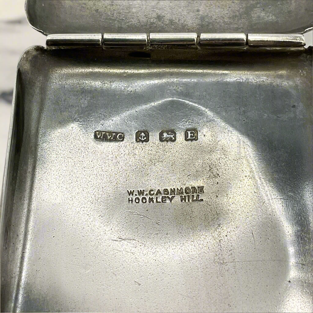 Close-up of open matchbook case with hallmarks on a marble surface.