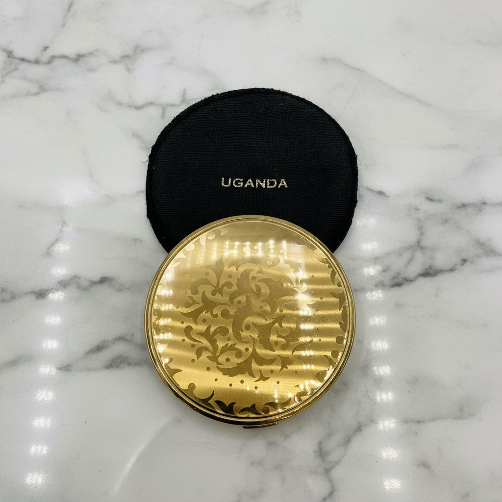 Gold compact mirror with intricate design on a marble background