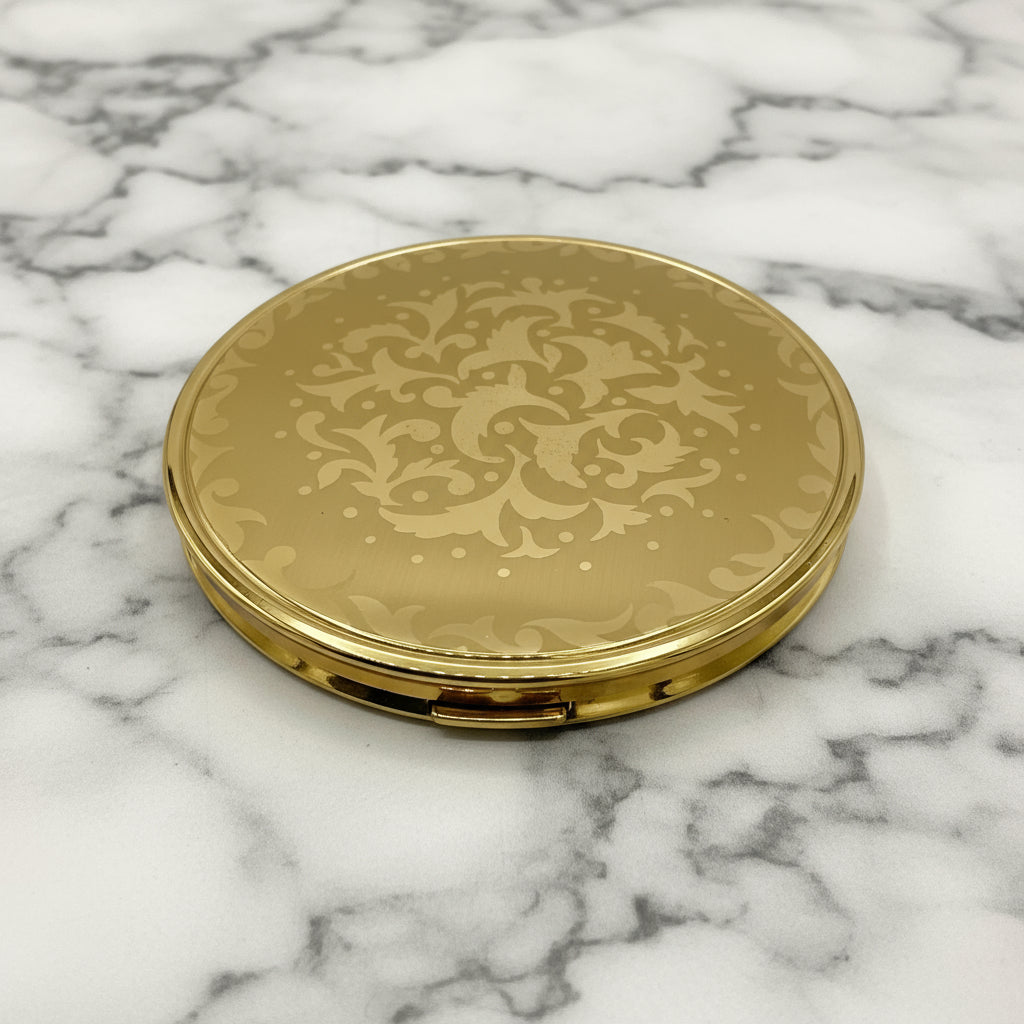 Gold compact mirror with decorative pattern on a marble background