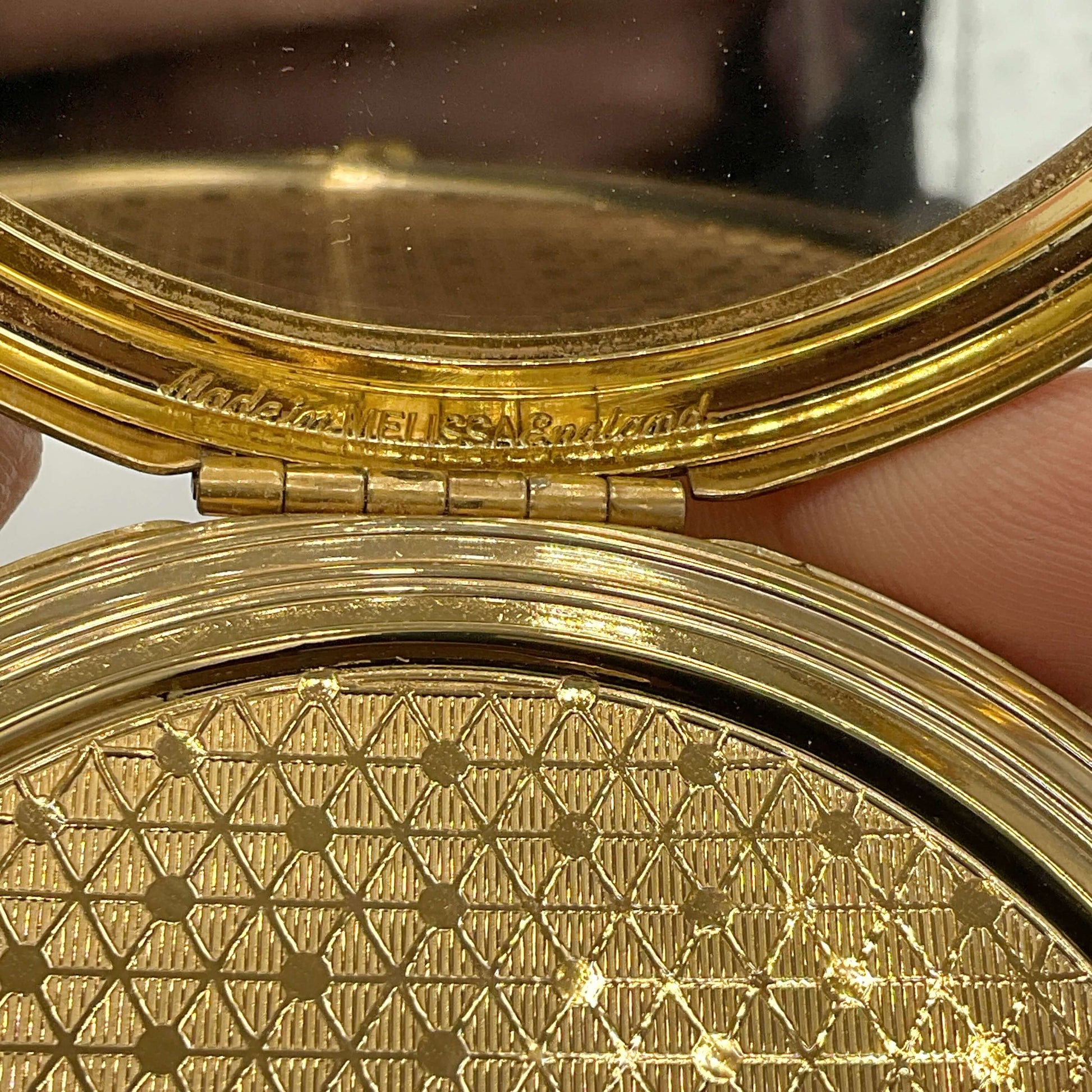 Close-up of a gold compact mirror with intricate design with Melissa and Made In England engraved 