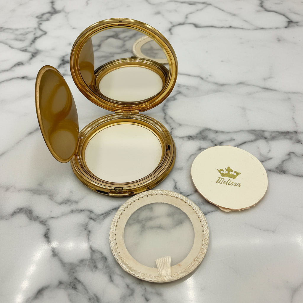 Powder Compact mirror with open lid, showing mirror, powder screen and Melissa powder applicator on a marble background 