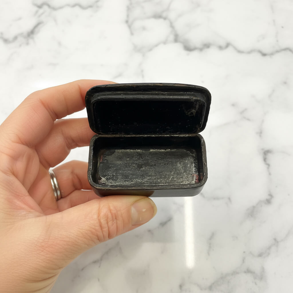 Hand holding a small black box against a marble background