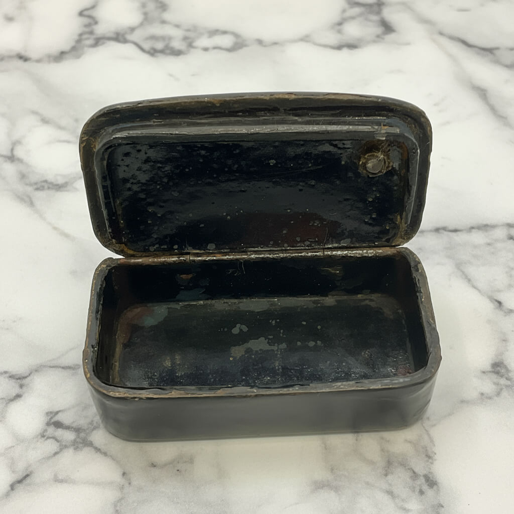 Black snuff box with an open lid on a marble surface