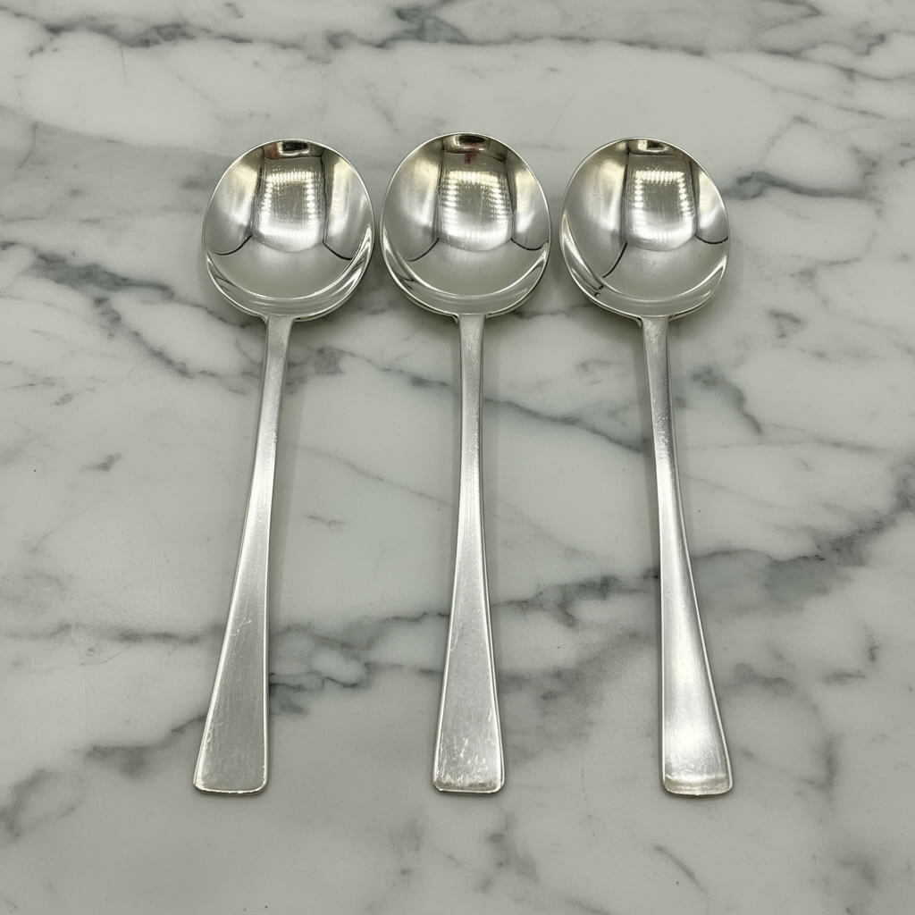 Three silver salt spoons on a marble surface