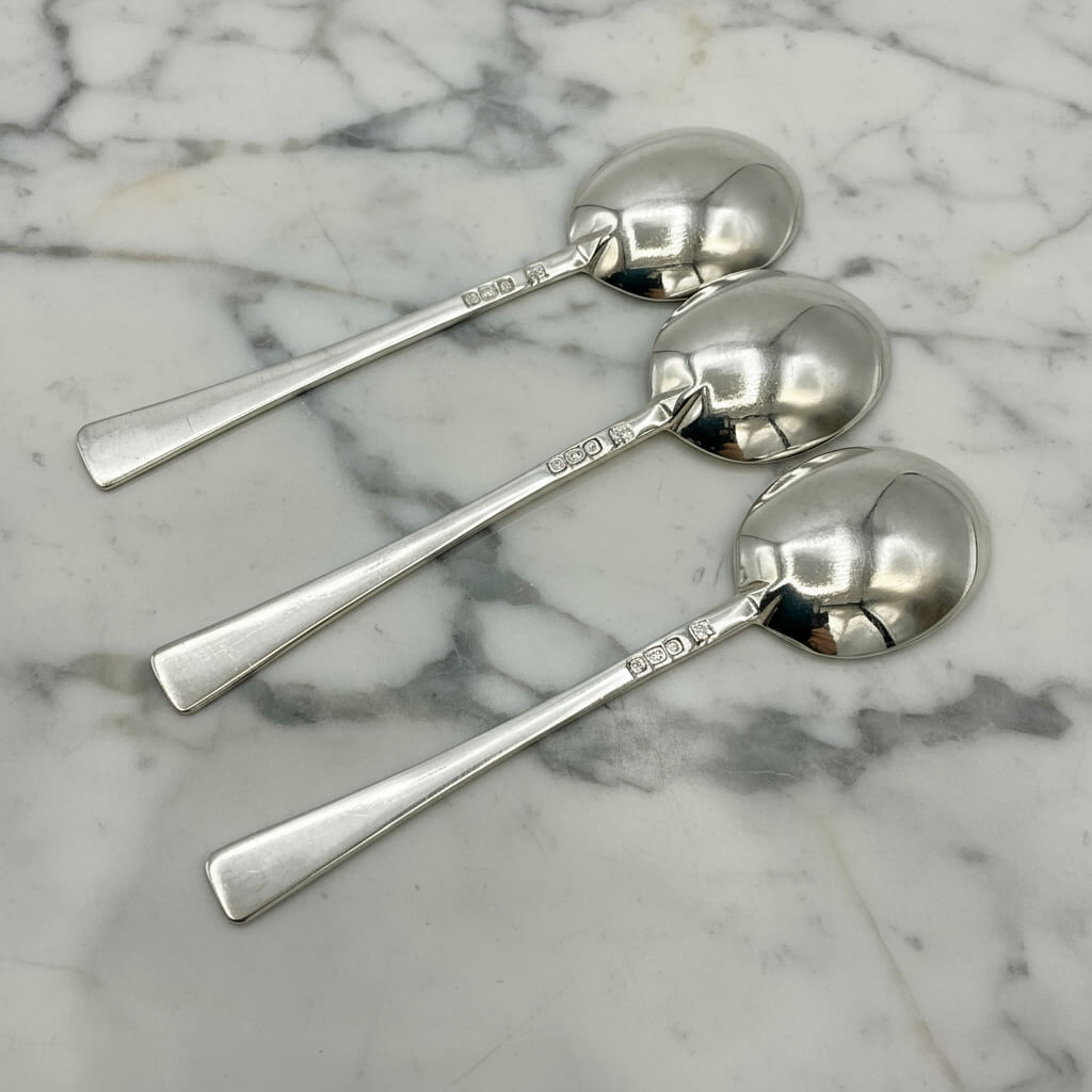 Three silver salt spoons on a marble surface