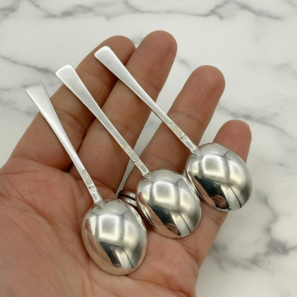 Set of three silver salt spoons held in a hand with a marble background