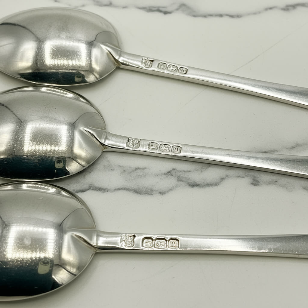 Three silver salt spoons on a marble surface