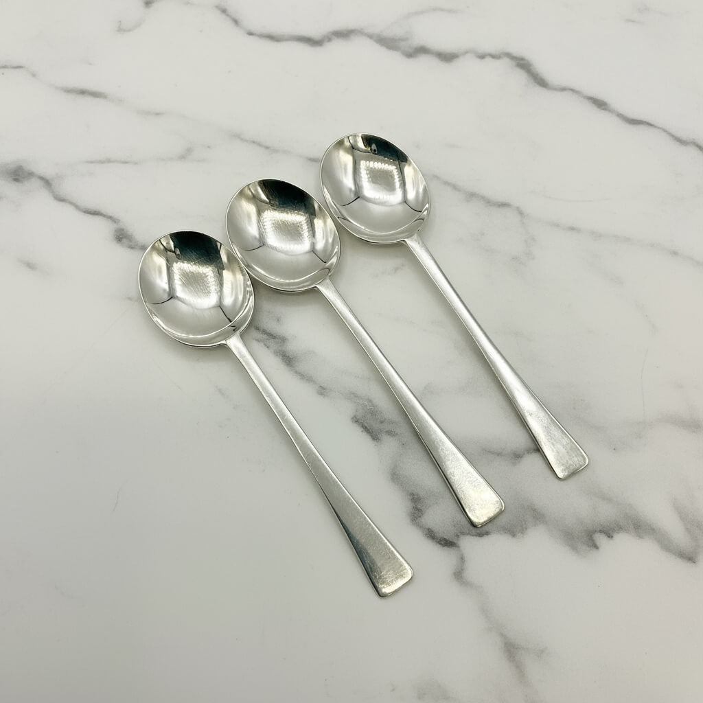 Three silver salt spoons on a marble surface